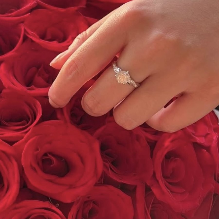 A newly engaged client's round diamond ring on her hand over a bouquet of red roses