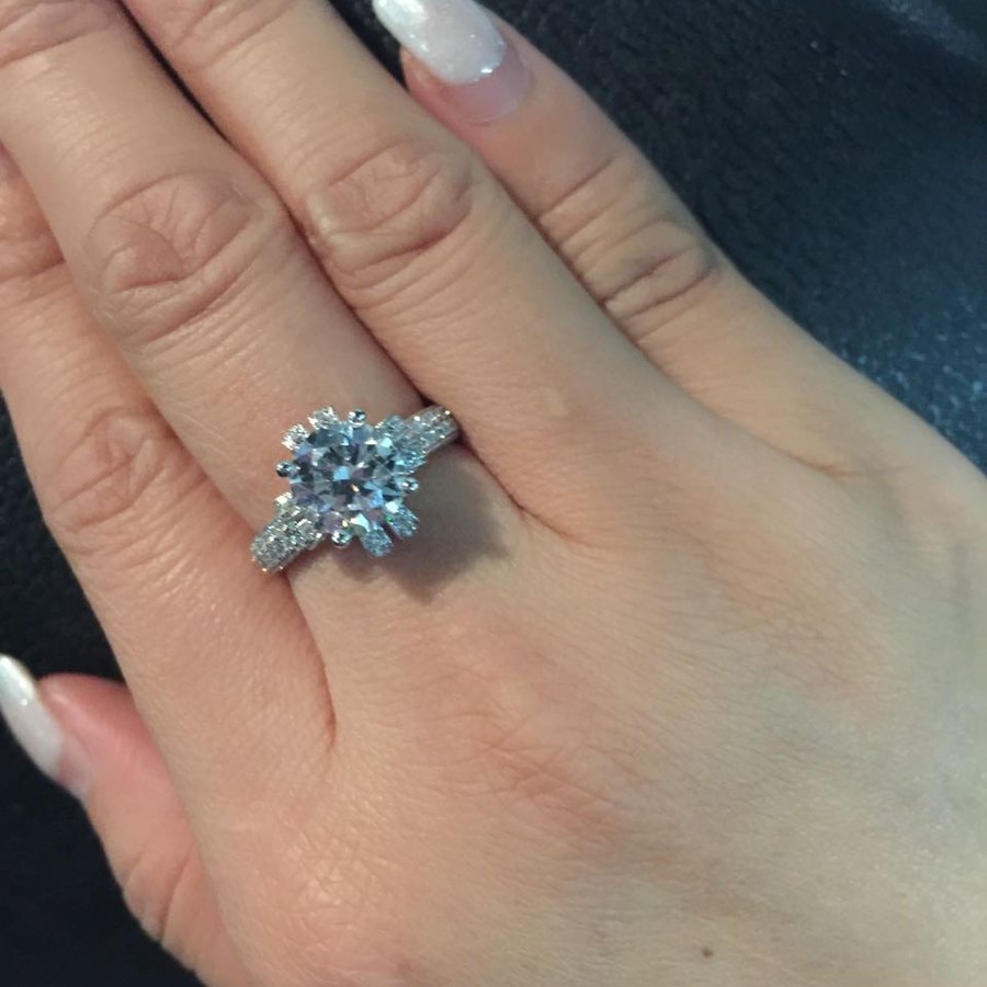 A round diamond ring with pavé shoulders worn on a hand