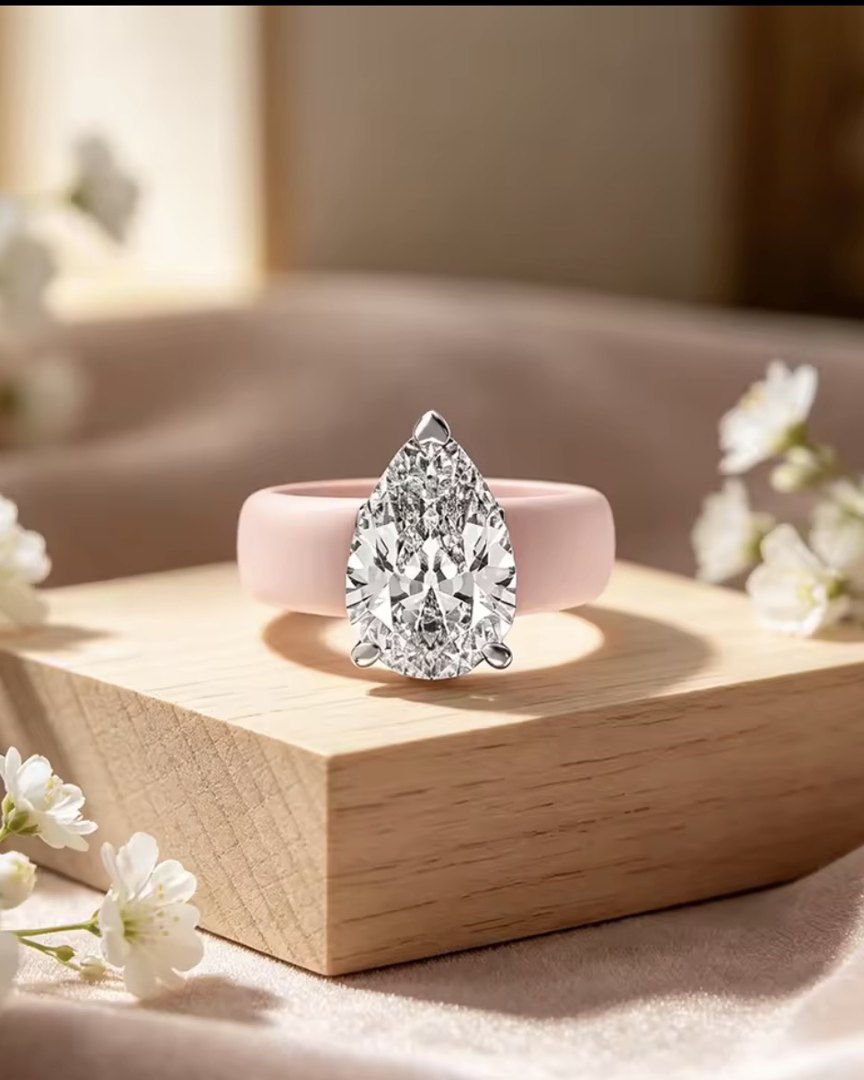 A pear-shaped stone set on a blush pink silicone ring band, resting on a wood block