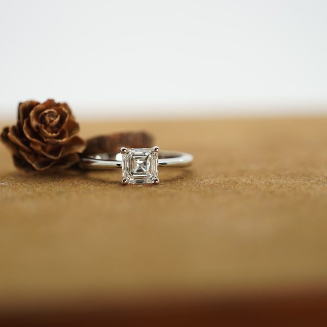 Asscher-cut diamond solitaire ring beside a dried rose
