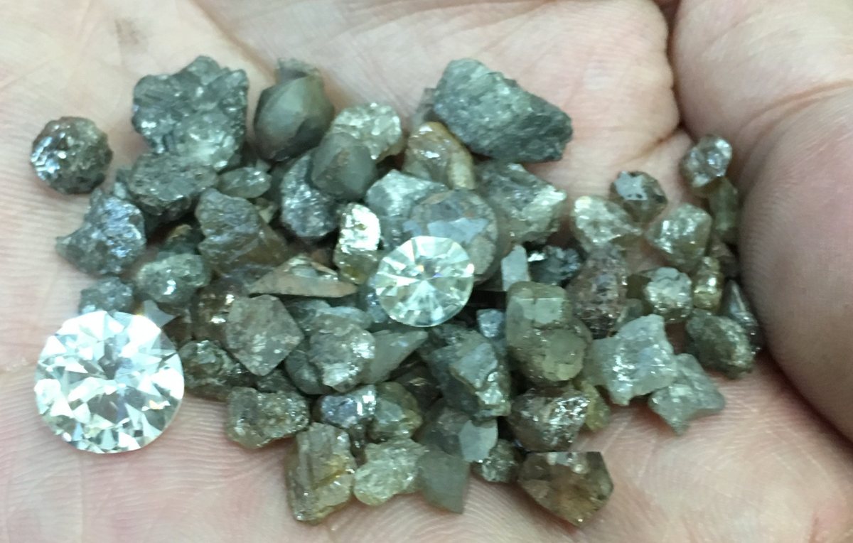 Grey and brown rough diamonds in a palm with two polished round diamonds